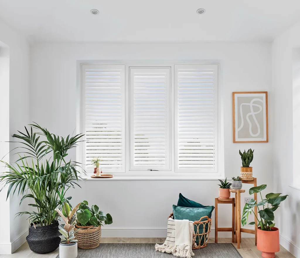 White Perfect Fit shutters in a bright living room surrounded by houseplants
