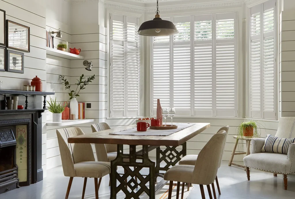 White plantation shutters in a dining room with a fireplace and pendant light