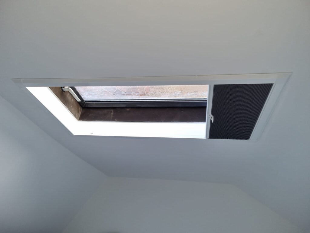 An open Velux roof window in a white-painted loft ceiling