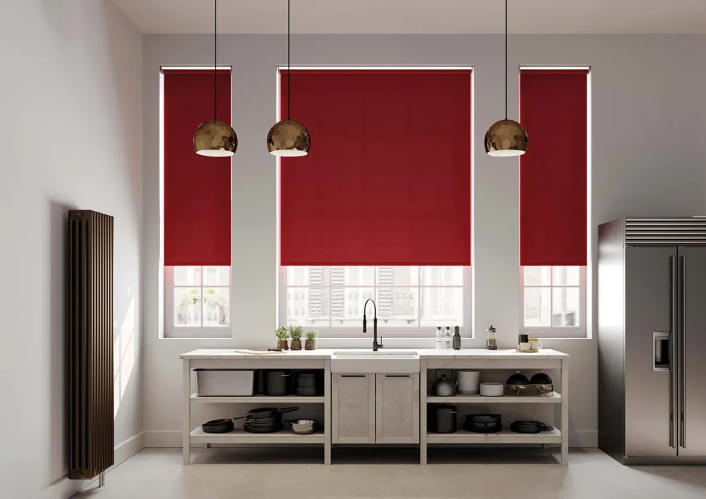 Deep red roller blinds fitted to three kitchen windows above a sink and worktop