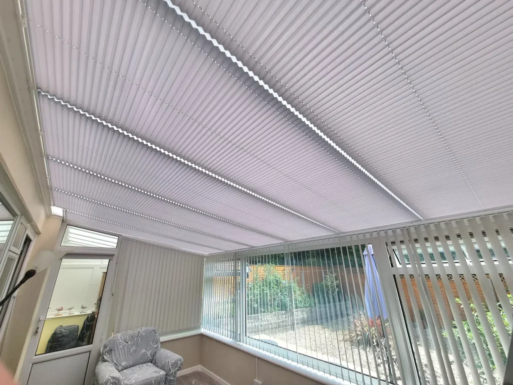 Pleated conservatory roof blinds seen from inside, with the garden beyond