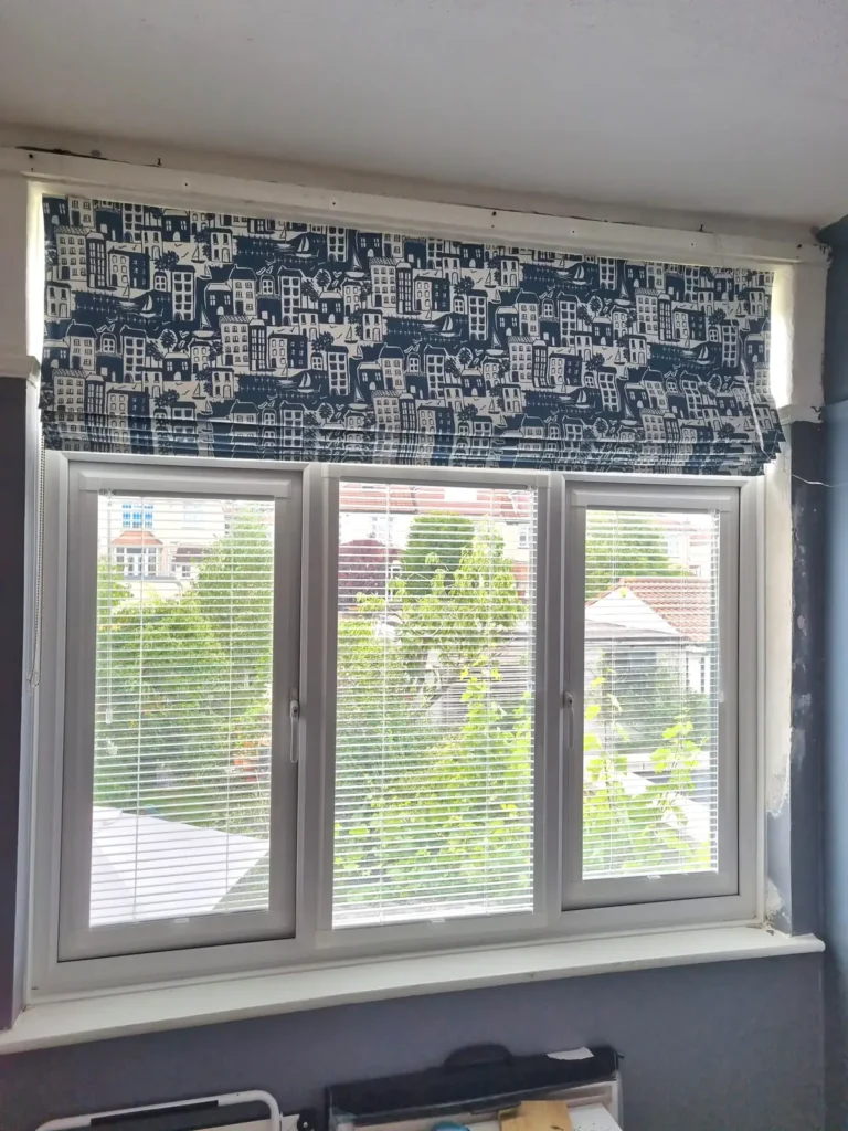 A navy patterned Roman blind fitted above white Venetian blinds
