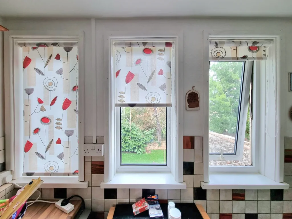 Patterned roller blinds on two kitchen windows with one casement tilted open