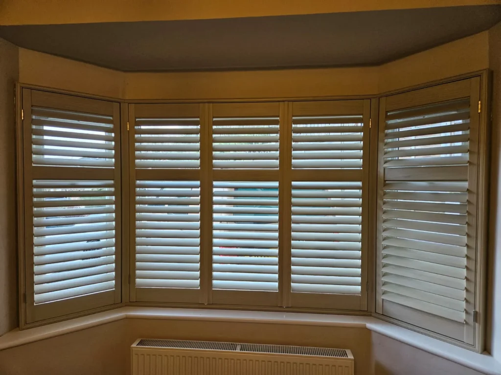 Cream plantation shutters across a bay window with the slats half open