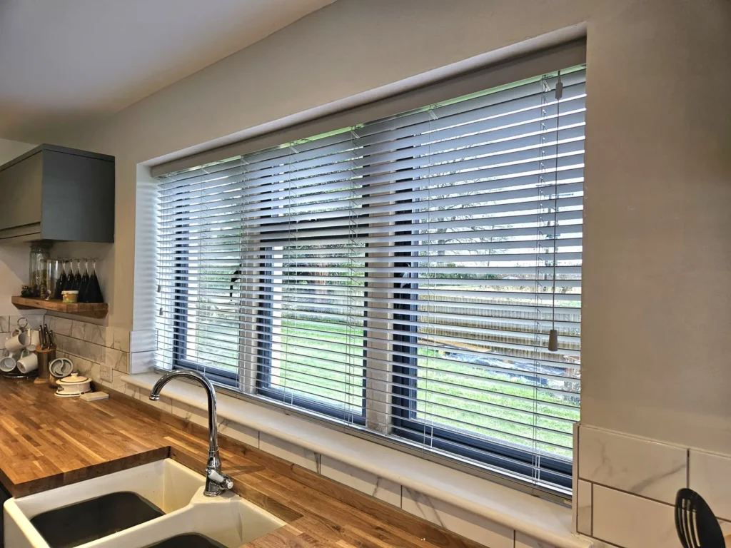 Wooden Venetian blinds above a kitchen sink looking out onto a garden
