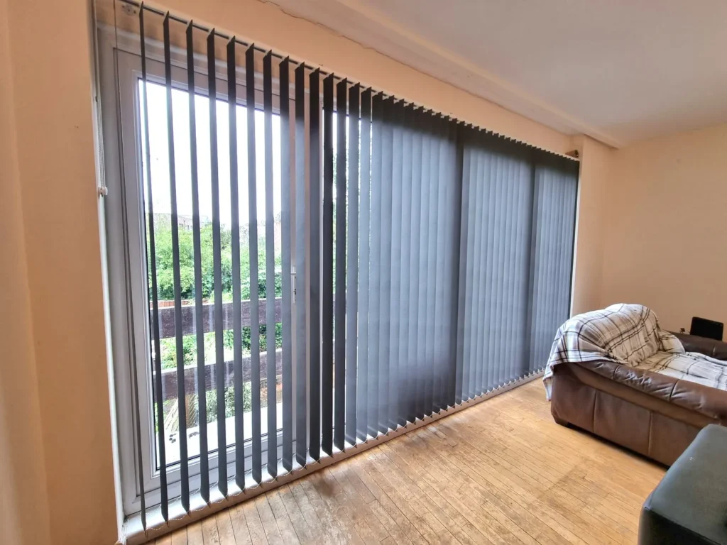 Grey fabric vertical blinds drawn across wide patio doors in a living room