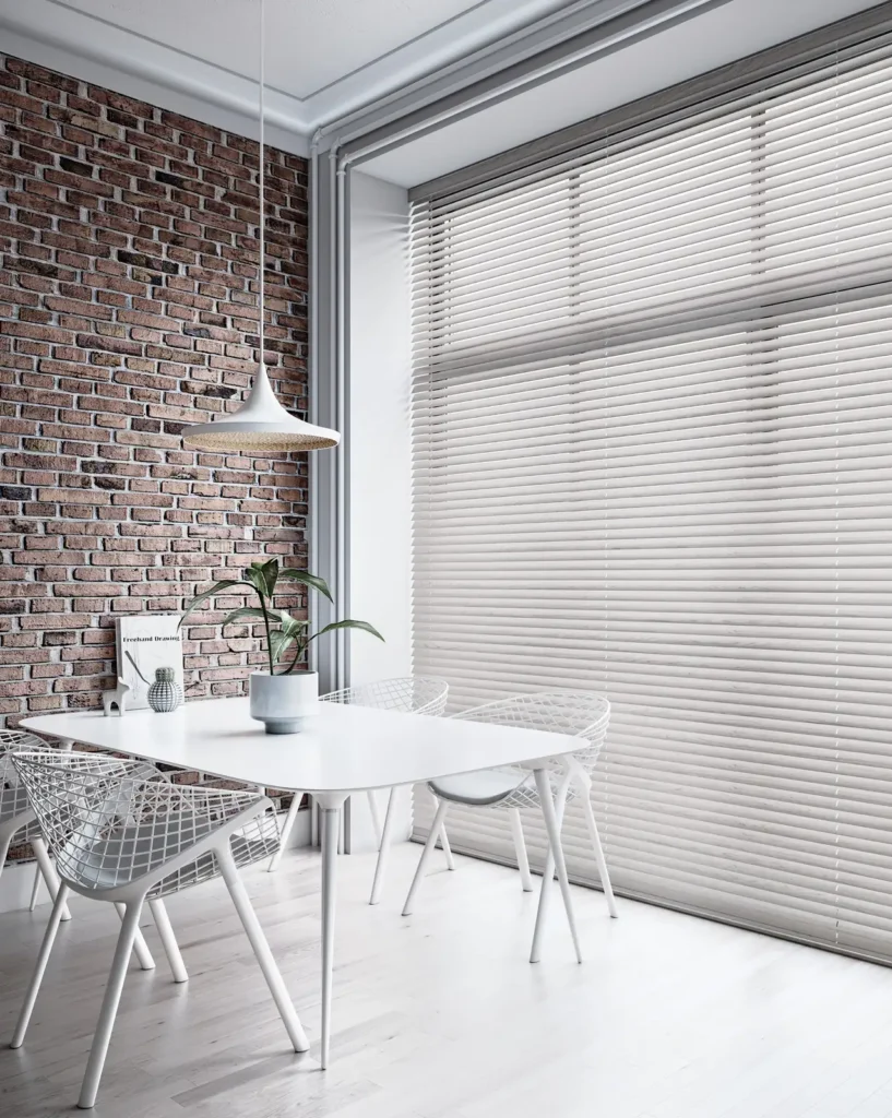 Slim white aluminium Venetian blinds across a dining room window with an exposed brick wall